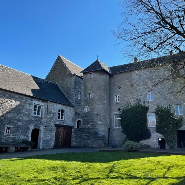 À propos Façade en pierre des Écuries de Beauregard à Wanze sous un ciel bleu.
